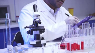 Hintli bilim adamı laboratuardaki panoda mikroskop ve yazı kullanıyor. 