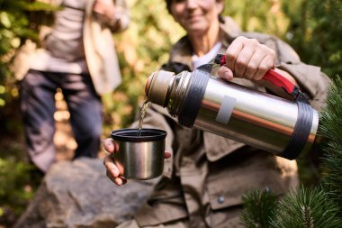 Üst düzey bir çift doğa macerasının tadını çıkarıyor. Yürüyüşleri sırasında sıcak bir içecek dolduruyorlar..