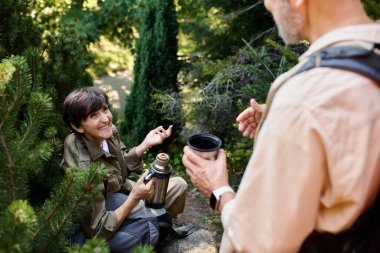 Kıdemli bir çift, yemyeşil bir ortamda yürüyüş yaparken, hikayelerini ve kahkahalarını paylaşırken mola verir..