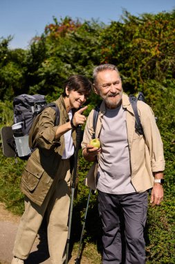 Yaşlı çift yürüyüş yolunda gülümsüyor, doğayla çevrili bir anı paylaşıyorlar..
