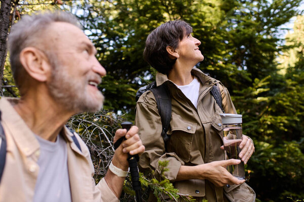 Пожилая пара наслаждается пешим приключением в окружении пышных деревьев и бурной природы.