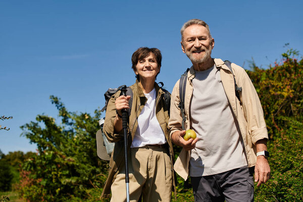 Active seniors explore nature together, sharing smiles and fresh fruit during their hike.