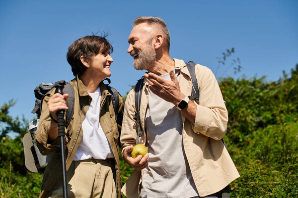 A senior couple shares a joyful moment while hiking in the mountains on a sunny day.