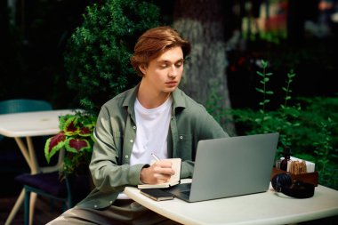 A young man dressed in a shirt using his laptop in a cozy, modern cafe.