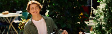 A young man in an olive green shirt smiles while enjoying his meal at a trendy cafe, banner