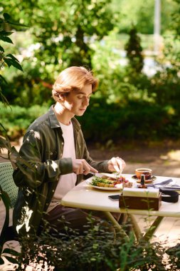 A young man in an olive green shirt savors his meal at a trendy cafe, enjoying nature.