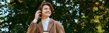A young man in a trendy coat smiles while walking in autumn park, banner