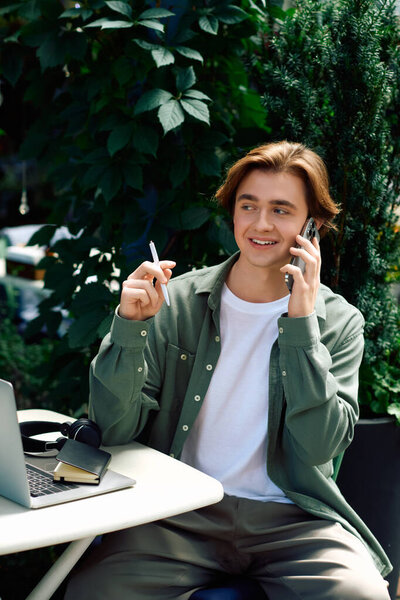 A young man in a shirt multitasks with a laptop and phone at a stylish cafe.