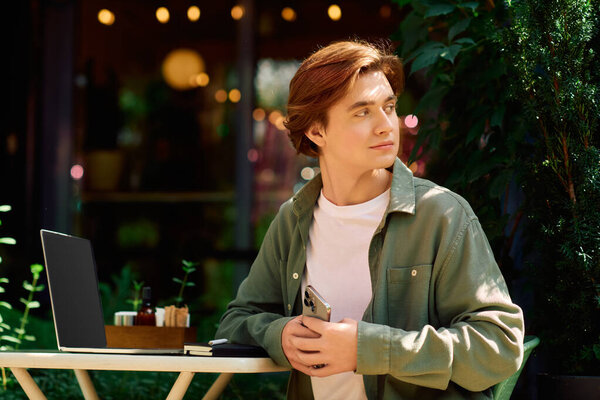 A young man sits in a cafe, using his laptop while enjoying the peaceful surroundings.