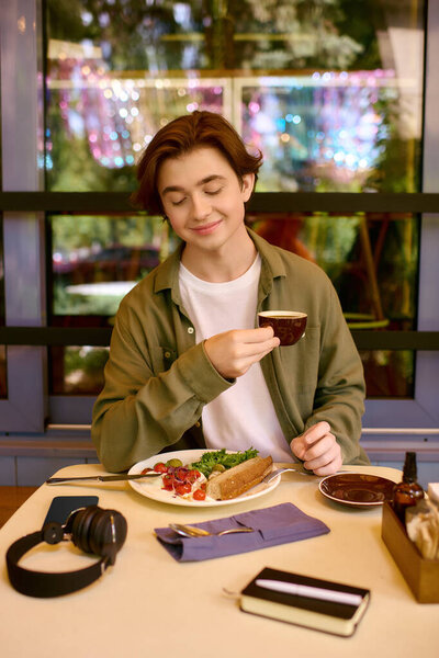 A young man wearing an olive green shirt savors his meal in a modern cafe setting.
