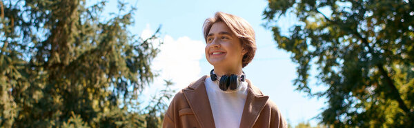 Bright autumn day finds a young man in a stylish coat wandering through a serene park, banner