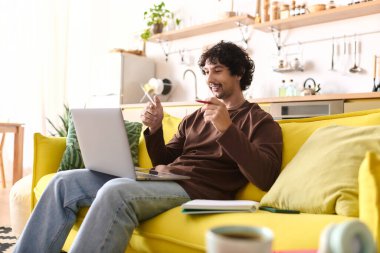 Young man interacts happily on a laptop from a comfortable spot in a sunny living space.