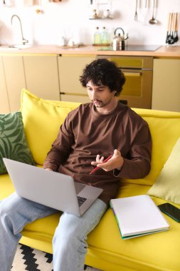 Handsome man engages with his laptop while seated comfortably on a vibrant yellow couch.
