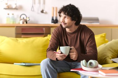 A young man sips coffee while contemplating in a bright, inviting space filled with warmth.