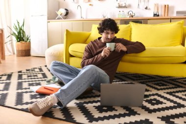 Young man relaxes with a cup of coffee, focused on his laptop in a stylish living room.