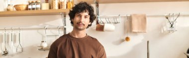 A young man stands confidently in a bright kitchen, surrounded by fresh ingredients and warm decor.