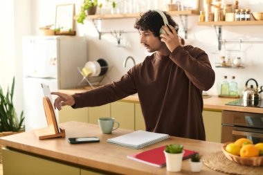 Handsome young man wearing headphones focuses on a tablet while enjoying a cup of coffee.