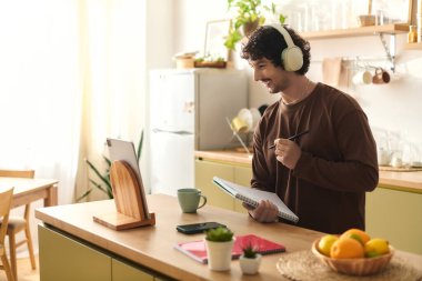 Handsome young man smiles while taking notes and making plans in a sunny kitchen setting.