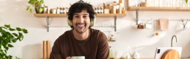 Young man smiles brightly as he sips a warm drink, surrounded by plants and soothing decor.