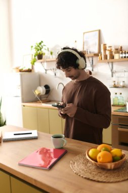 A handsome young man is in a modern kitchen, absorbed in his phone, enjoying a peaceful morning.