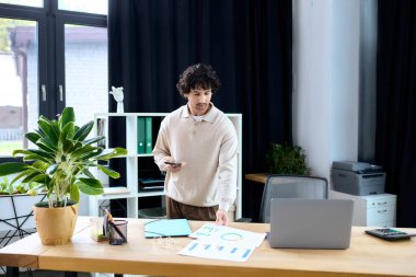 Young man with curly hair engages with papers and phone in bright, stylish workspace.