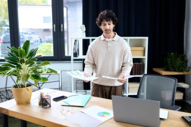 Focused young man reviews data charts while standing in a stylish office environment.