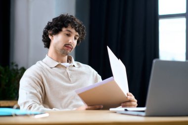 Young man focuses on his paperwork while sitting comfortably at a desk during the day.