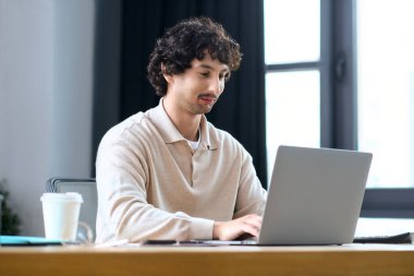Young man focuses on his laptop, enjoying a productive day in a well lit office.