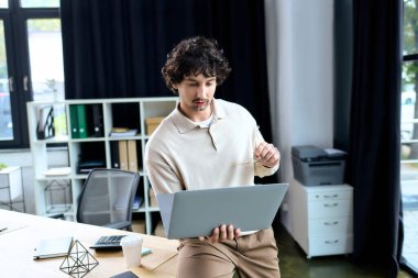 Handsome young man focused on his laptop while adjusting his glasses in a stylish office.