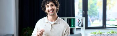 Handsome young man engages in conversation while using a laptop in a bright workspace.