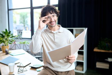 A handsome young man appears joyful as he examines paperwork in a bright, inviting office.