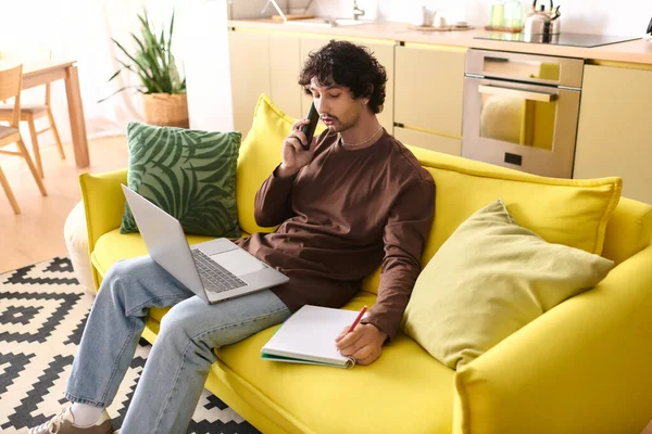 Handsome young man talks on the phone and takes notes on a cozy yellow sofa at home.