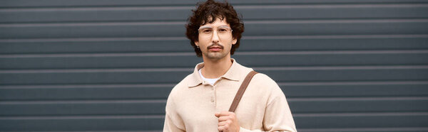 Handsome young man stands with a relaxed demeanor, showcasing his trendy fashion choices.