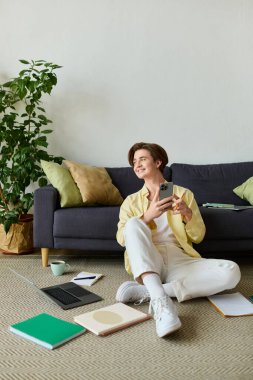 Şık bir genç adam, sıcak bir yaşam alanında akıllı telefonuyla koltuğun yanında oturuyor..