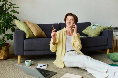 Şık bir genç adam telefonda konuşurken gülümsüyor, rahat bir şekilde oturma odasında oturuyor..