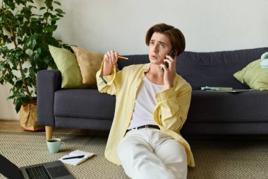 Şık giyinmiş genç bir adam yerde rahatça otururken telefonda sohbet ediyor..