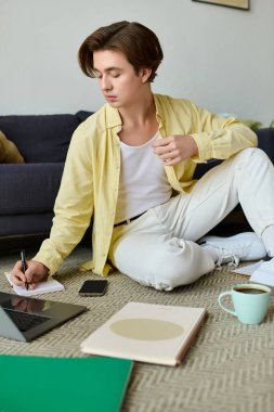 Yakışıklı genç adam, etrafı sanat malzemeleriyle çevrili yerde rahatça otururken notlar yazıyor..