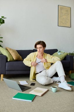 Tarz sahibi genç adam laptopuyla, notlar ve fincanla çevrili işine odaklanıyor..