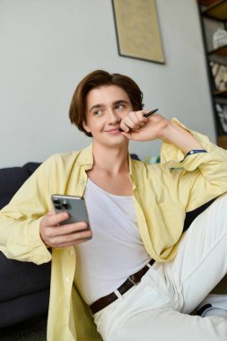 Düşünceli bir ifadeye sahip genç bir adam rahat bir yaşam alanında akıllı telefonuyla iletişim kuruyor..