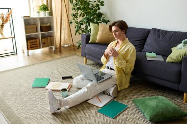 Şık bir genç adam dizüstü bilgisayarına odaklanmış kitaplarla yerde oturuyor..