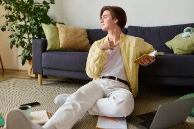 Genç yakışıklı adam yerde rahatça oturuyor, bir defter ve kalemle ilham alıyor..