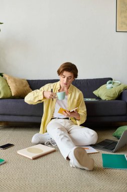 Genç bir adam rahatça yerde oturur, içkisini yudumlar ve etrafı kitap ve aletlerle çevrilidir..