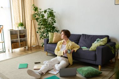 Şık bir genç adam rahat bir şekilde yerde oturur, parlak, davetkar bir yerde çayını yudumlar..