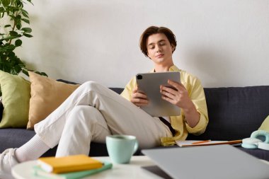 Modayı takip eden genç adam rahat bir kanepede dinleniyor, tabletine sarılmış ve defterleri yakınlarda..