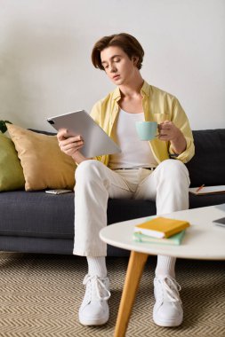 Şık bir adam kanepede rahatlar, kahvesini yudumlar ve rahat bir odada tabletini karıştırır..