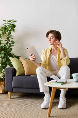 Şık bir genç adam kanepede dinlenir, tabletle meşgul olur ve fikirleri hakkında düşünceli olur..