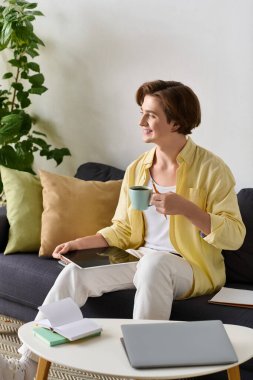 Genç adam rahat bir şekilde kanepede oturur, kahvesini yudumlar ve yumuşak yastıklarla çevrilidir..