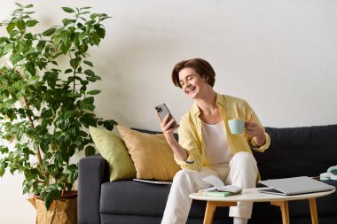 Şık bir genç adam rahat bir kanepede, elinde kahve ve telefonuyla rahatlar..