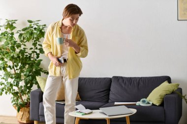 Havalı genç adam kahveyi yudumluyor ve rahat bir kanepe ve yeşil bitkilerin yanında uzak bir işe girişiyor..