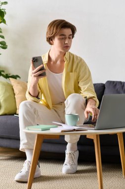 Yakışıklı genç adam elinde akıllı bir telefonla dizüstü bilgisayarıyla evde dinleniyor..